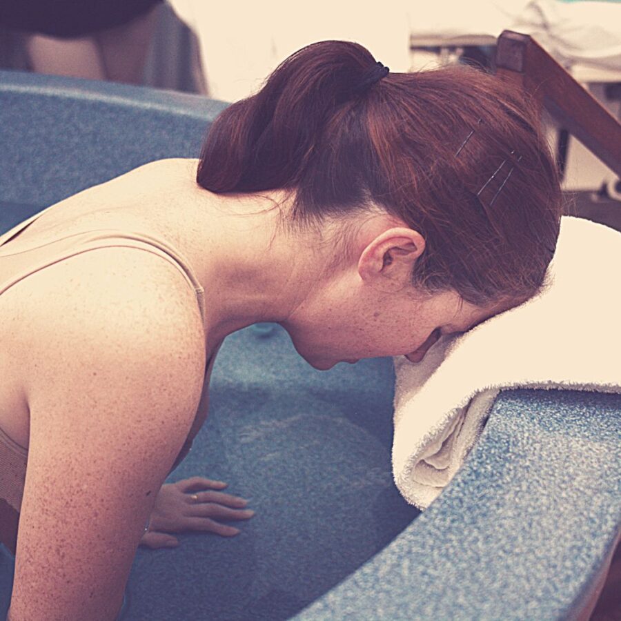woman in water birthing tub with head leaned on the side of tub on a towel