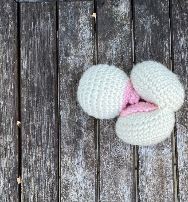 crochet breast and mouth, zoomed in, off white colored yarn with pink nipple and pink tongue, on a brown faded background