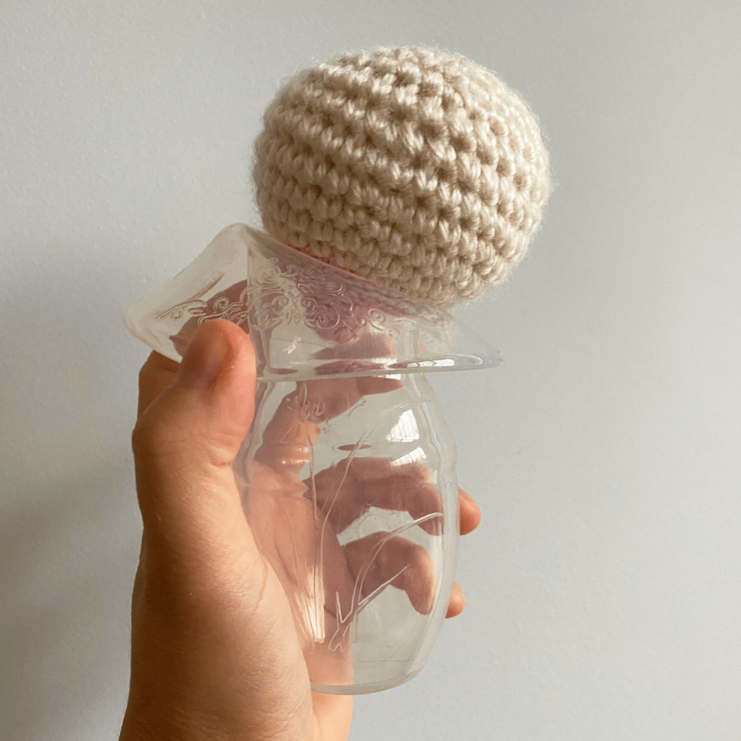 haakaa silicone breast pump in woman's hand with wall as the background, edges pulled back and crochet breast with nipple pointing to middle of haakaa silicone pump